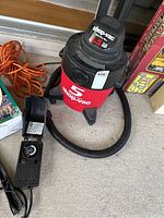 Photo of red and black Shop-Vac vacuum with attached hose and orange power cord visible.