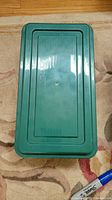 Top view of dark green plastic storage bin lid on carpet