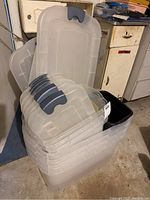 Clear plastic storage totes with dark gray lids stacked with a small black trash can inside one of the totes. Used condition with minor wear visible.