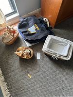 Overall lot view showing tote bags, nesting baskets, and shell-decorated woven baskets on grey carpeted floor by window and wooden cabinet.