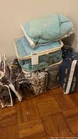 Stack of six towels in protective bags and fabric zippered cases in colors such as light blue, grey, and patterns.