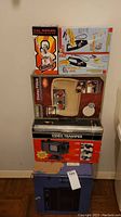 Full set of items stacked against wall: heating pad, Cal Ripken bobblehead box, pocket fishing toy box, video transfer machine box, slide projector.