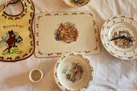 Photo showing Bunnykins bib, hot plate, teaching clock, egg cup, and one bowl with bunny illustrations all laid out on a flat surface.