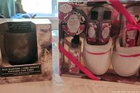 Photo showing wax painted candle in box and slippers and lotion set in packaging with pink ribbon.