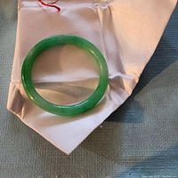 Top-down view of green jade bangle resting on white satin pouch
