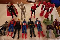 Photo of eleven Marvel superhero action figures arranged on beige surface with white, red backing for some figures.