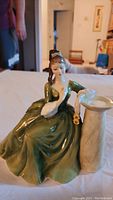 Front view of the Royal Doulton figurine showing the seated woman in green dress next to column.
