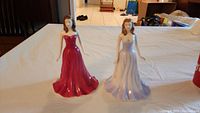 Both Royal Doulton figurines together on a table, showing red and lavender gowns.