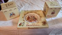 Royal Doulton Bunnykins Celebrate Your Christening plate in original packaging with two Bunnykins mugs in original boxes arranged on cloth surface.
