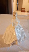 Front view of glossy porcelain seated woman figurine in light dress with arms crossed over lap.