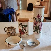 Photo of five decorative items including Wedgwood creamer, Crown Ducal candy dish, Bluenose Nova Scotia plate, Weatherby Hanley Falcon Ware floral vase, and tall fruit-illustrated jar with wooden lid.