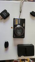 Top view of Sony Cyber Shot camera with lens covers and USB card reader and charger on white background.