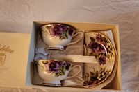 Two porcelain teacups and two saucers in original box, with floral and gold detail.