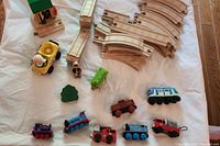 Top down view photo showing an array of wooden Thomas and Friends themed trains including a green tanker, multiple engines and train cars, as well as curved and straight wooden train track pieces and a green tree accessory.