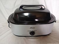 Oster 18 quart roaster oven shown assembled with black high dome lid and silver body with temperature control knob.