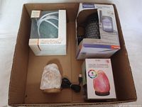 Overview of the four items in the lot inside a cardboard box: two essential oil diffusers in packaging, one raw Himalayan salt lamp, one boxed color-changing salt lamp.