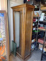 Side view of tall wooden display cabinet with glass door showing wood frame and molding details.