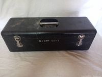 Full front view of the black Floating Pal tackle box, showing rectangular shape, built-in handle lid, metal latches, and the name 'Ralph Levy' on front surface.