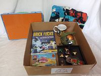 Box with miscellaneous LEGO items including mini-figures, a LEGO base plate, a book, and a coffee mug