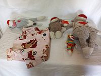 Four sock monkeys of varying sizes and two pink sock monkey patterned robes laid out on white bedding.