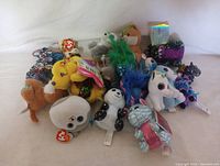 Multiple clip animal plush toys arranged together showing variety of characters and colors like yellow bird, panda, unicorn, and sequin animals.