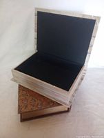 Open hollowed-out book with black interior sitting on another book, showing interior storage space and birch bark styled exterior.