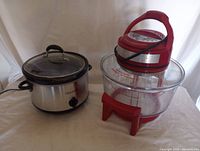 Photo showing both the Crock-Pot slow cooker with glass lid and stainless steel body, and the Sharper Image digital oven with clear glass bowl and red plastic lid and base