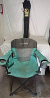 Front view of one green and gray Magellan Outdoors camping chair with a carrying bag standing behind it