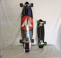 Photo showing both skateboards side by side with longboard on the left and short board on the right, displaying their size difference and deck graphics.