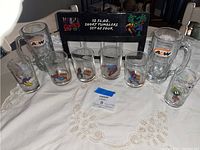 Photo showing 4 Marvel Comics shot tumblers, 2 A&W glass mugs, and 4 Looney Tunes character glasses displayed on white cloth.