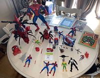 Overall view of the Spider-Man collection on a round white table, showing the large tall Spider-Man figure, helicopter toy, Spider-Man comic book and record, and assorted figures.
