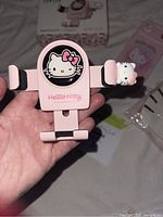 Close-up of pink Hello Kitty car mount holder with Hello Kitty face logo and adjustable arms featuring Hello Kitty figurines.