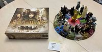Overview photo of the Lord of the Rings board game box with the circular figure circle setup next to it.