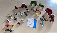 Top-down view of all vintage micro mini vehicles and farm tractors arranged on the floor, showing red farm tractors with trailers, multiple miniature cars in blue, yellow, red, and white, several miniature airplanes, and small boats.