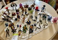 Photo showing diverse collection of collectible figures including action figures, animals and toys laid out on a white lace tablecloth