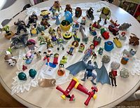 Top view of multiple toys and figures arranged on a table displaying variety of characters from popular franchises with mixed small items and figures.