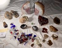 Full view of all rocks, geodes, and polished stones laid out on fabric, showing variety of types and sizes including large pink agate bookends, amethyst cluster, and sea glass pieces.