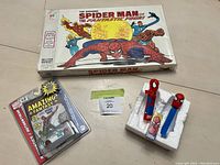 Photo showing the Spider-Man board game box, two vintage Spider-Man PEZ dispensers in styrofoam packaging, and the new sealed Marvel Amazing Fantasy toy vehicle in original blister pack.