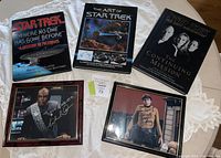 Photo showing three Star Trek books and two framed autographed photos on a white lace tablecloth.