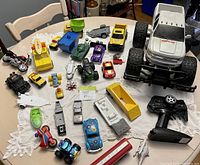 Full lot view showing the assortment of toy vehicles including the large white remote control 4x4 truck, smaller cars, motorcycles, and other vehicle toys on a table