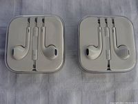 Two sets of Apple wired earphones with white cases placed on a cloth background, displaying the earbuds, remote and cable neatly coiled.