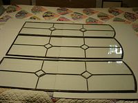 Three leaded glass window panels laid on a quilted surface, showing full front view and rounded top corners on two panels.