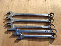 Photo showing five combination wrenches laid flat on wooden surface with visible rust and wear.