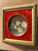 Frontal image showing the entire framed floral painted plate on red velvet backing within an ornate gold frame.