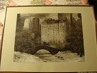 Framed lithograph depicting a snowy Central Park scene with stone bridge and buildings in background.