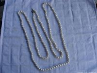 Full view of the pearl necklace laid out on a blue cloth, showing the entire length and pearl strand with knots between each pearl.