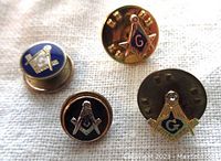 Front view of four small Masonic pins showcasing enamel colors and metal details.