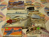 Photo showing overall lot of vintage plastic model kits with 1970s box art on quilted surface.