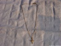 Full view of 10K gold chain necklace with cross pendant laid out flat on fabric.
