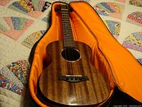 Full view of Rosen concert ukulele inside a padded bright orange interior soft case, showing wood grain finish and strings.